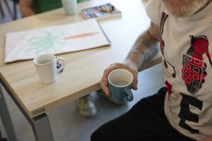 Een mannelijke bewoner van De Geuzenhoek met een tatoeage op zijn rechterarm heeft een kopje water vast.