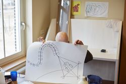 Een kale man houdt een grote tekening voor zijn gezicht met daarop een vlieger getekend met een gezicht.