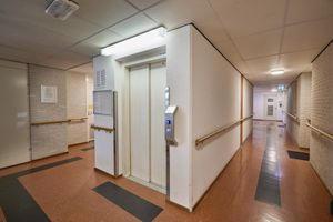 Gang met een open lift, leuning, plafondverlichting en een bruine vloer.