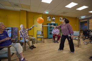 Een groepje mensen speelt ballontennis vanuit zit op een stoel.
