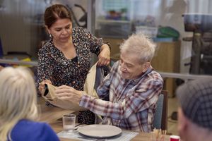 Een vrouw helpt een man bij het uittrekken van zijn jas zodat hij kan gaan eten.
