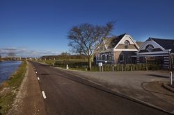 Een oud landgoed met witte details aan de gevel langs een autoweg en een kanaal. Daarboven helder blauwe lucht.
