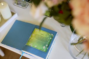 Een open boek met een pagina met bloemenmotief ligt op een tafel, omringd door kaarsen en met wazige roze bloemen op de voorgrond.