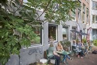 Mensen zitten aan tafels buiten een gebouw, genietend van het mooie weer.