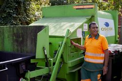 Een man met een oranje fluoriscerende outfit drukt op een knop van een grote groene afvalverwerkingsmachine.