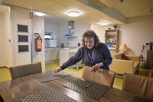 Een vrouw met grijze trui en wild bruin haar dekt een tafel in een woonkamer met keuken.
