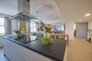 Moderne keuken en eethoek met een strak kookeiland, bloemstukken, houten stoelen en grote ramen die zorgen voor veel natuurlijk licht.