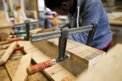 Iemand in een blauwe trui, maakt lijmklemmen vast aan stukken hout.