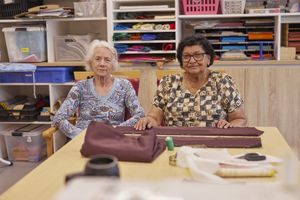 Twee wat oudere dames buigen zich over een bruin stuk stof in het textielatelier.