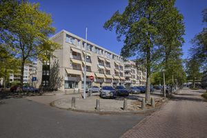 Vier verdiepingen tellend woongebouw met balkons en geparkeerde auto's aan een straat met bomen.
