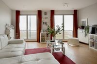 Ruim opgezet appartement met veel licht. De inrichting is voornamelijk wit van kleur en erg strak en modern. Er staan ook nog wat kamerplanten in de kamer.