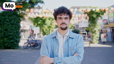 Een jonge man met donker haar staat op straat en kijkt krachtig in de camera. Linksboven staat het logo van Mo Online.