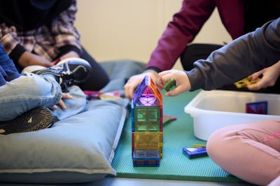 Kinderen bouwen een kleurrijke constructie met magnetische tegels op een blauwe mat.