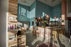 Gezellig restaurant met aquablauwe muur, houten tafels en stoelen, en een bar met gekleurde tegelprint.