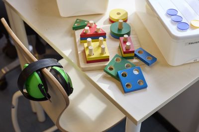 Houten vormpuzzels en groene koptelefoon op een tafel naast een stoel, in een lichte binnenruimte.