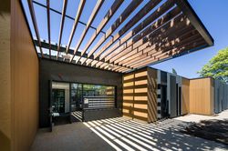 Een gelijkvloers gebouw met groot afdak van houten latten. De deur van de ingang staat open en daarnaast zijn zo'n 30 brievenbussen.