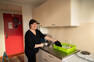 Persoon doet een zojuist afgewassen bord in het afdruiprek en kijkt lachend naar de camera