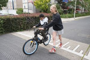 Een kind rijdt op de fiets en begeleider de duwt hem vooruit