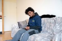 Persoon zit op een zitbank met de telefoon in beide handen en kijkt in gedachten