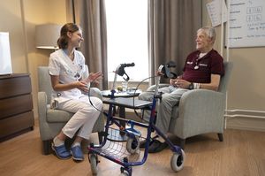 Zorgmedewerker zit tegenover cliënt met daarnaast een rollator