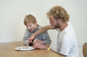 Begeleider helpt een kind met eten met een vork