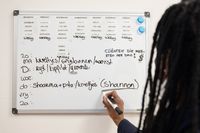 Iemand schrijft het weekmenu op een whiteboard aan de muur.