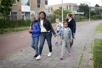 Drie kinderen en twee begeleiders wandelen op straat hand in hand