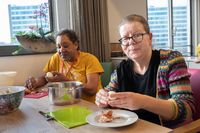 Een donkere man met zwart kroeshaar en een blanke vrouw met bril pellen ontspannen een ei voor de lekker salade. Op tafel staat een pan, een snijplank en een schaal voor de salade.