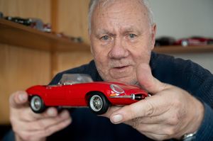 Een oudere man toont vol trots zijn felrode sportauto in miniatuurformaat.