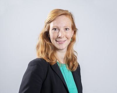 Portret van een jonge vrouw met halflang rood haar. Ze lacht vriendelijk en draagt een groene top met een zwarte colbert.