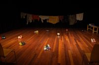 Een toneel met daarop verschillende paren schoenen met een bloem erop. Achterin hangt een waslijn vol met kleding.