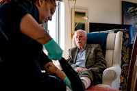 Thuiszorgmedewerker trekt sokken van oudere man uit die in stoel zit