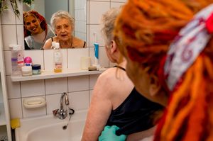 Thuiszorgmedewerker staat achter oudere dame in de badkamer en ze kijken samen in de spiegel