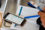 Een smartphone waarop een app wordt weergegeven, ligt op een tafel met een pen en papier, waarop aantekeningen staan.