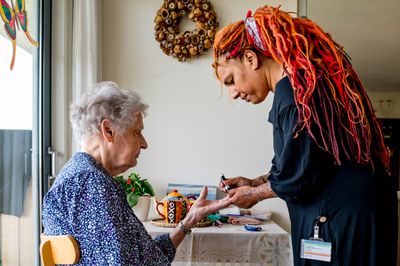 Thuiszorgmedewerker prikt bloed bij een oudere dame