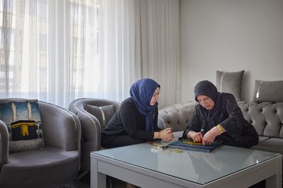 Twee dames met een hoofddoek maken een schilderij met spijkers en garen.