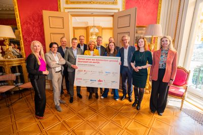 Een groen van 12 mensen staat in een chique zaal met in het midden in hun handen een bord. Op het bord staan logo's, handtekeningen en de tekst 'Samen eten we Amsterdam gezond, duurzaam en eerlijk'.