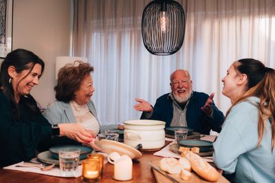 Vier mensen van uiteenlopende leeftijden zitten samen aan de eettafel met een pan met soep en lachen met elkaar.