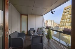 Modern balkon met rieten meubels, planten en uitzicht op hoge gebouwen. Glazen balustrade en houten vloer versterken de gezellige sfeer van de buitenruimte.