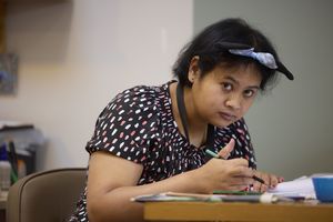 Een vrouw met kort zwart haar en Minnie Mouse haarband is aan tafel aan het kleuren.