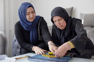 2 dames met een hoofddoek maken een schilderij met spijkers en garen.
