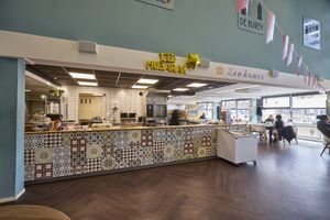 Een licht caféinterieur met een toonbank van mozaïektegels en mensen die aan tafels zitten.
