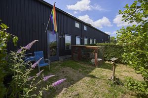 Een woning met een regenboogvlag en een tuin waarin gras ligt, een kippenhok staat en een vogelhuisje.