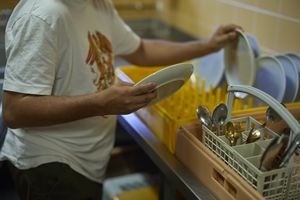 Een persoon haalt schone vaat uit de rekken.