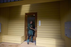 Een man open de gezamenlijke voordeur, in aan weerszijden zijn bankjes gemaakt aan de muur.