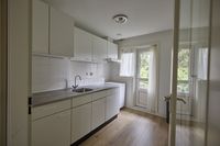 De keuken van een woning, de vloer is van hout, de kastjes zijn wit en er is een deur naar het balkon.