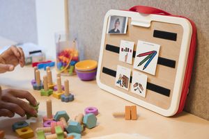 Kinderhanden spelen met houten speelgoed op een tafel, vlakbij een bord met plaatjes.