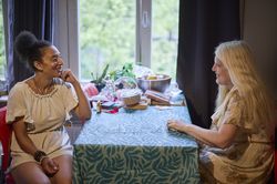 Twee bewoonsters zitten aan een tafel en zijn met elkaar in gesprek. Ze kijken elkaar aan.