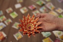 Een hand houdt een papieren bloem omhoog, gemaakt van oranjerode theezakjes