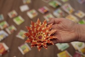 Een hand houdt een papieren bloem omhoog, gemaakt van oranjerode theezakjes